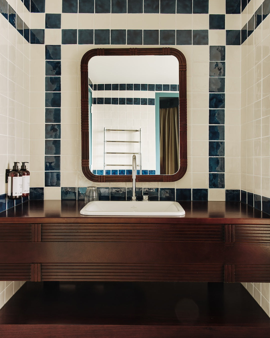 Salle de bain d'hôtel et flacons de soin Alaena posés au bord de la vasque